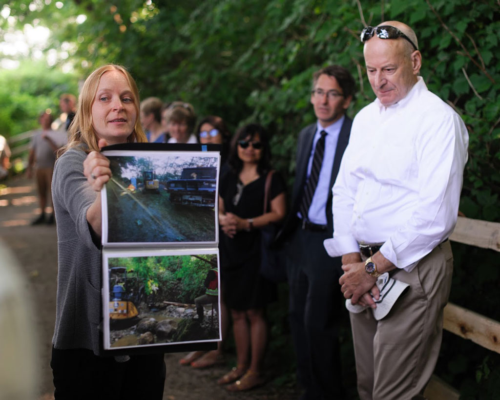 A Metro Vancouver biologist holds up a picture of various stages of the Salish Creek restoration.