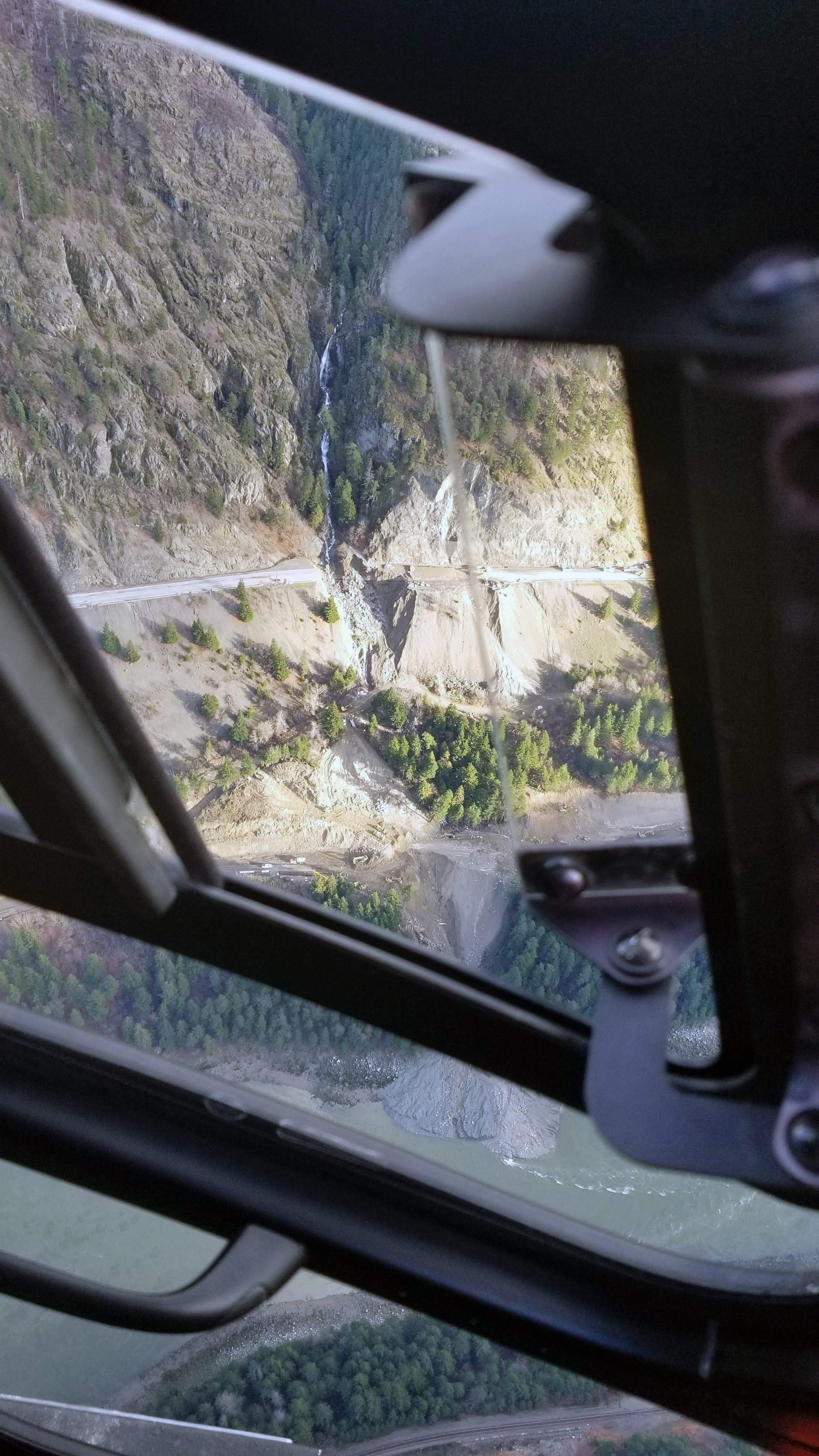 A highway cutting across the side of a mountain is cut in two due a river flowing faster and stronger than normal.