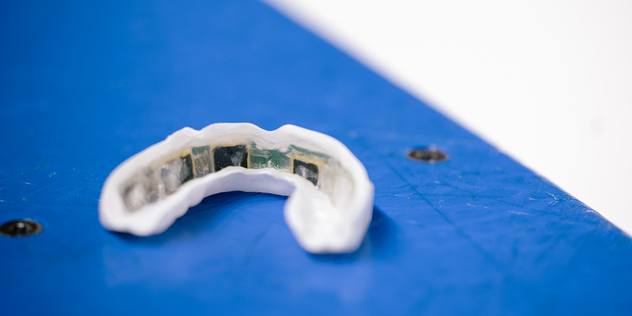 The inside of a mouthguard filled with IMG sensors is displayed on the edge of the ice-arena boards