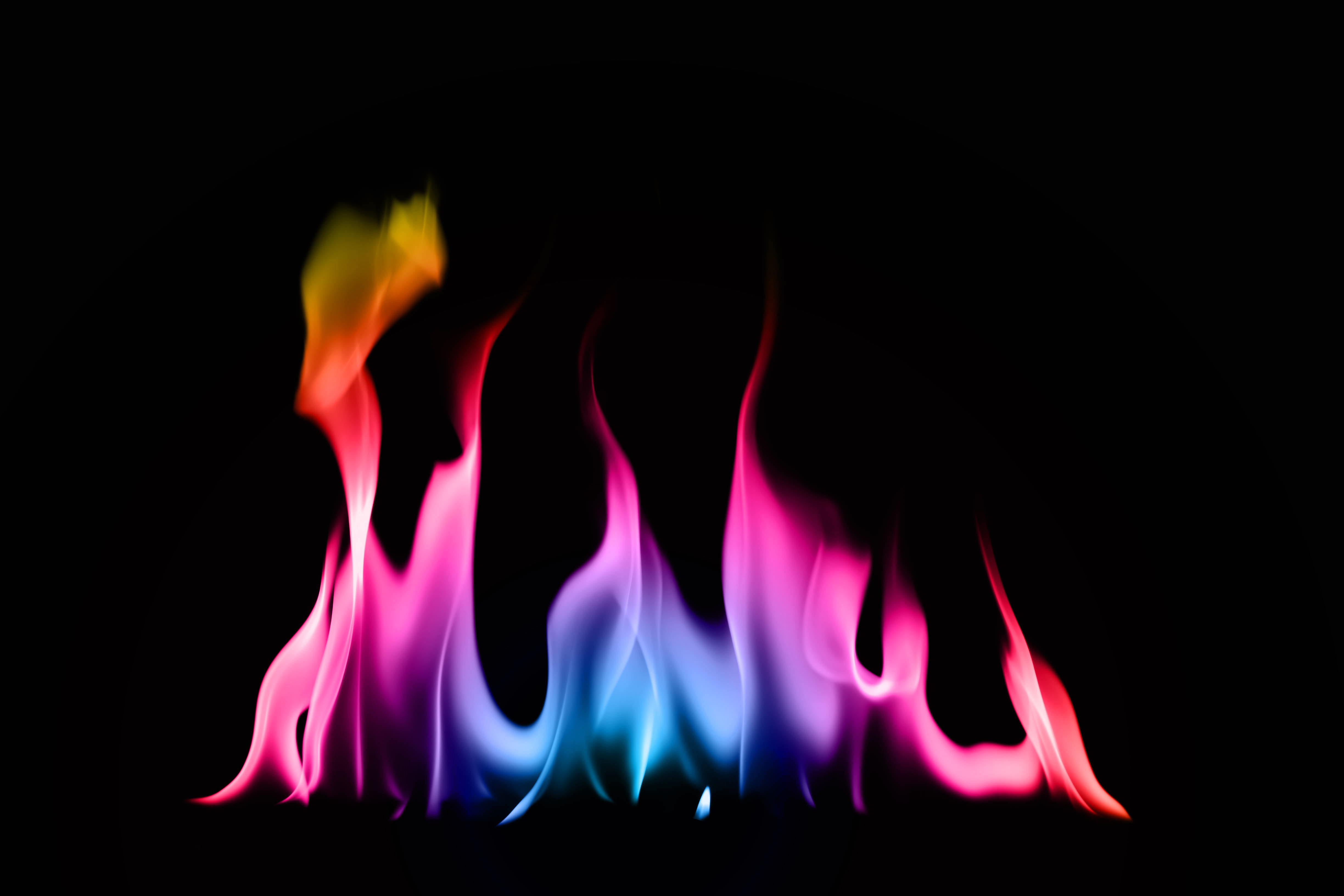 a rainbow fire of blue, pink, orange, yellow and purple flames burns against a black background. 