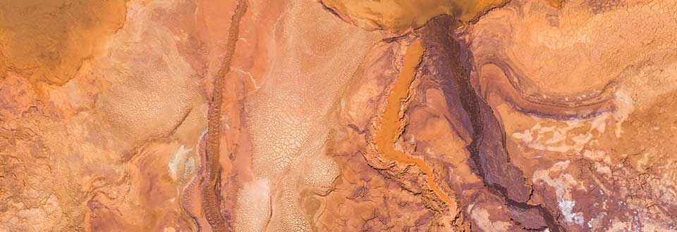 Aerial view of a mining site with rusty orange soil and streaks of darker minerals.