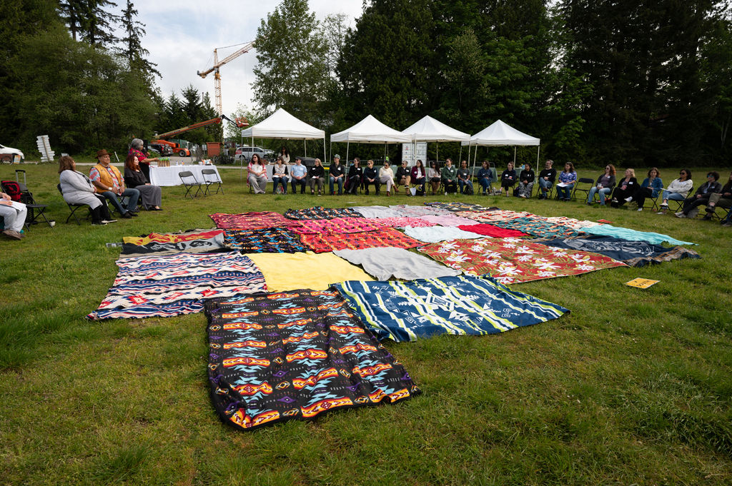 Participants sitting in a circle around various patterned blankets laid out in the middle