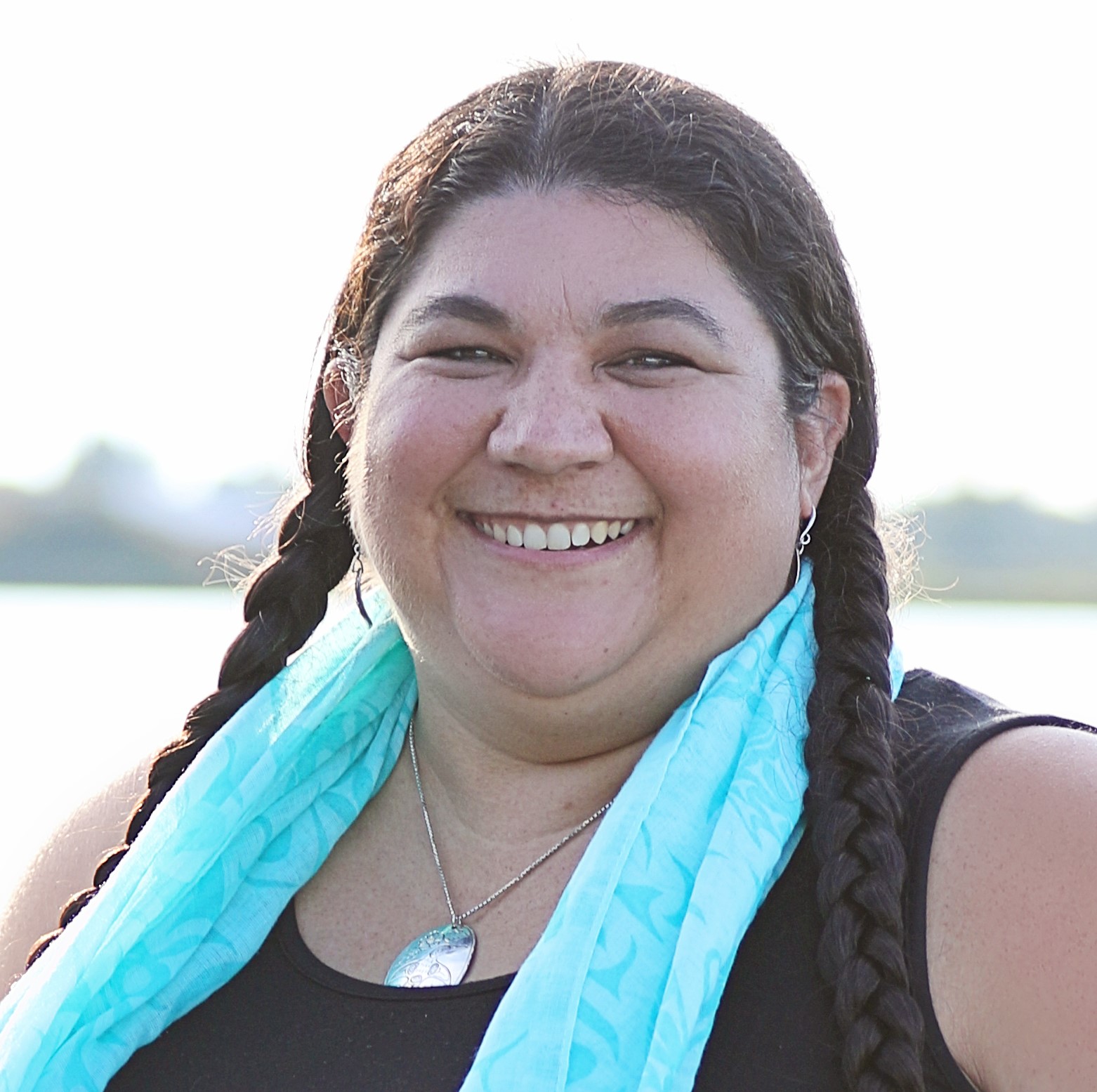 Headshot of Rhiannon Bennet, who wears a blue scarf around her neck and has two braids in her hair