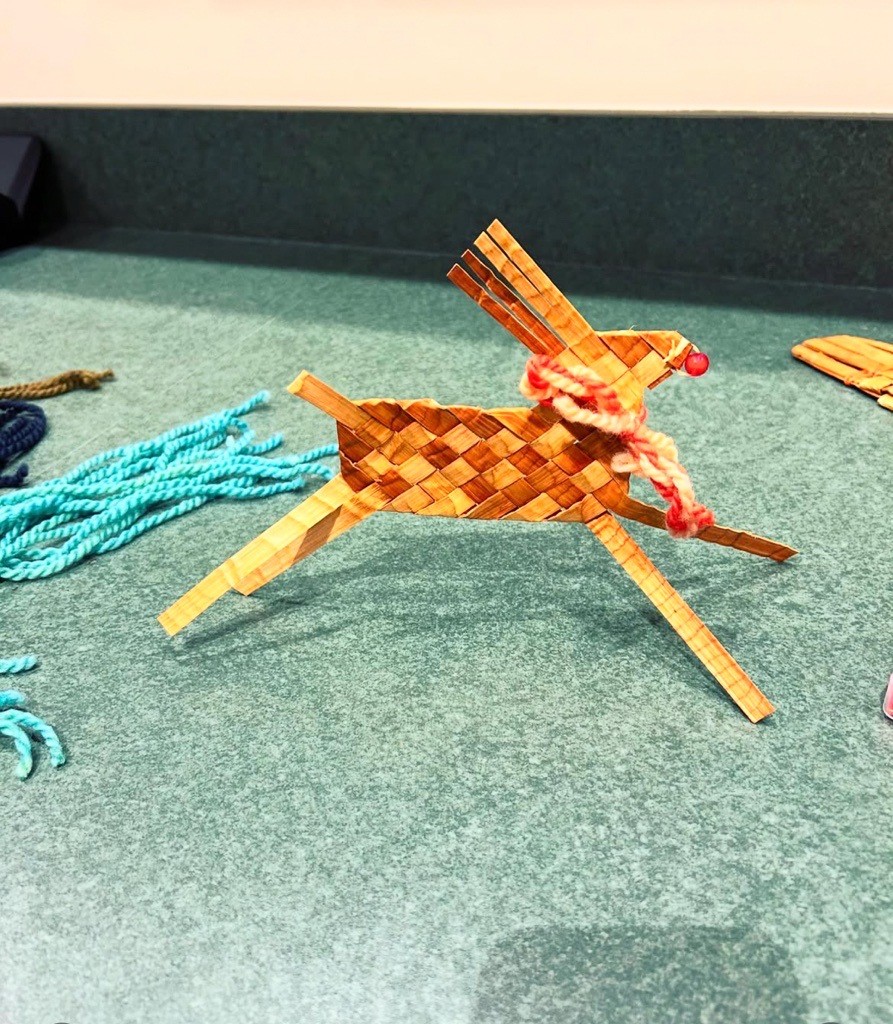 A depiction of a reindeer made by cedar weaving placed against a turquoise background