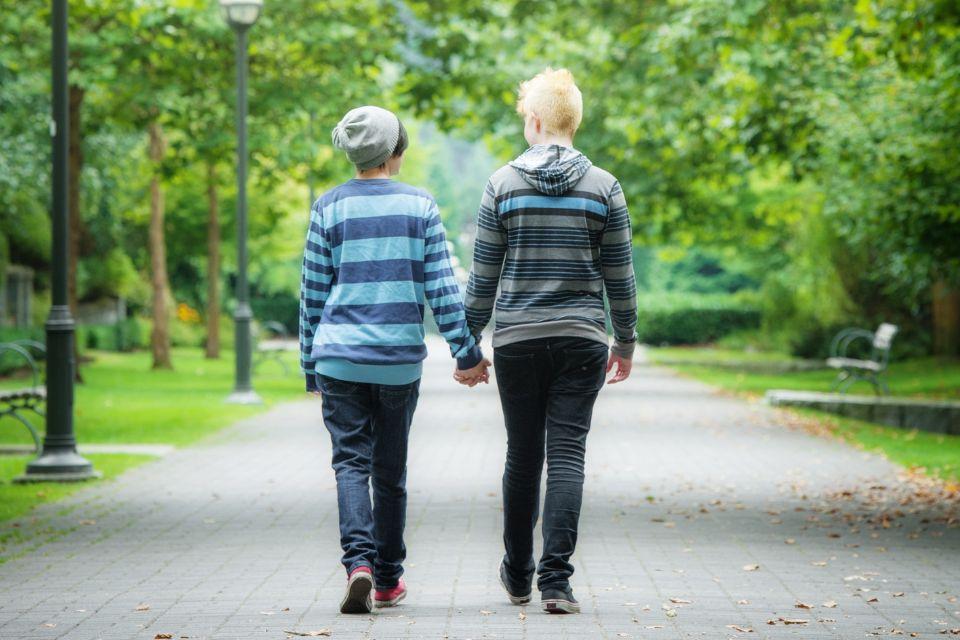 Two gender-diverse youth walking hand-in-hand in a park