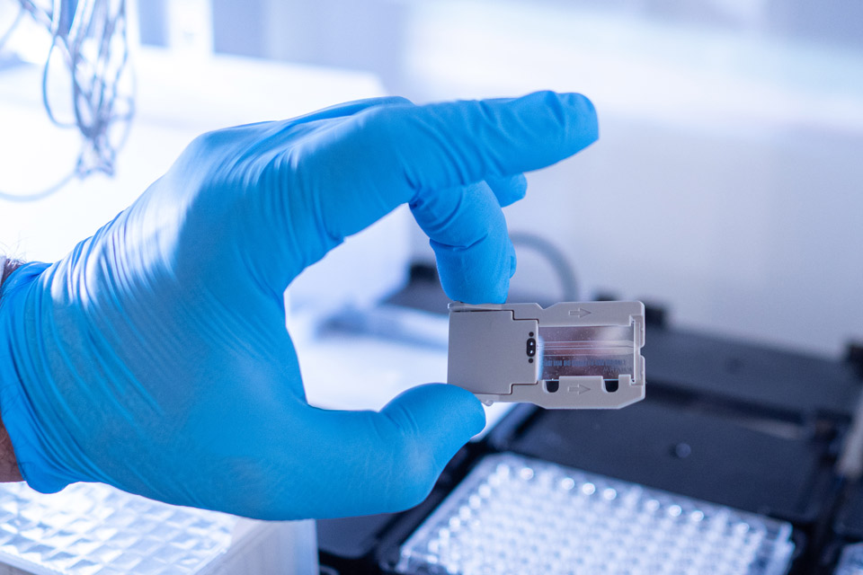 A hand wearing a blue latex glove holds a cartridge