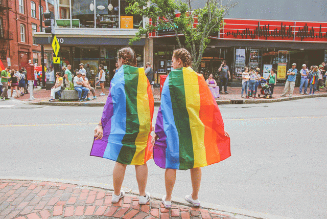 Two women wear rainbow flags on Congress Street in Portland, Maine during the annual Pride paradeTwo women wear rainbow flags on Congress Street in Portland, Maine during the annual Pride parade