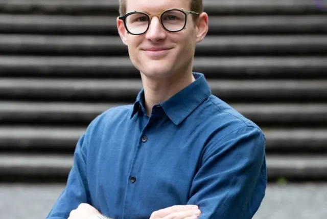 Man in glasses, folding arms in front of stone staircase