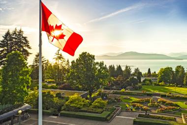 Aerial view of the UBC Campus in glowing summer light as the Canada flag waves in the foreground