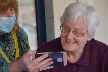 Old granny smiling at a phone that is being held by a nurse with a mask
