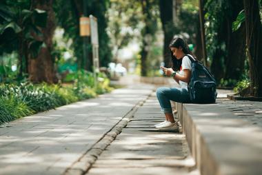 Woman sitting on pavement steps outdoors, looking at phone while waiting