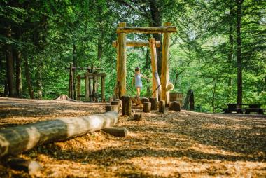 A child balances on a log in a shaded play area.