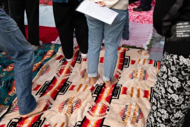 People standing on multiple patterned blankets laid out on the ground