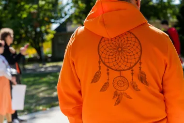 The back of a person wearing an orange hoodie with a screen-printed dreamcatcher design