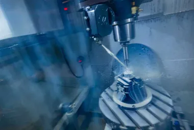 Close-up of a CNC machine drilling a metal part, with coolant spray visible.