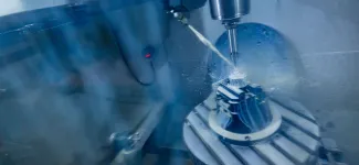 Close-up of a CNC machine drilling a metal part, with coolant spray visible.
