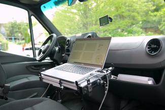 A view from inside the front interior of the PLUME van. A laptop with an air quality monitoring dashboard is accessible from the passenger seat. 