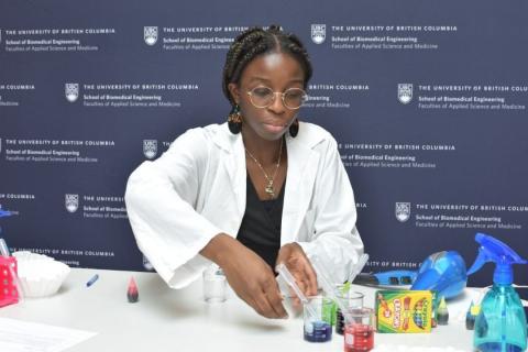 Coralie Tcheuné wearing a lab coat arranges beakers of brightly coloured liquid on a work bench