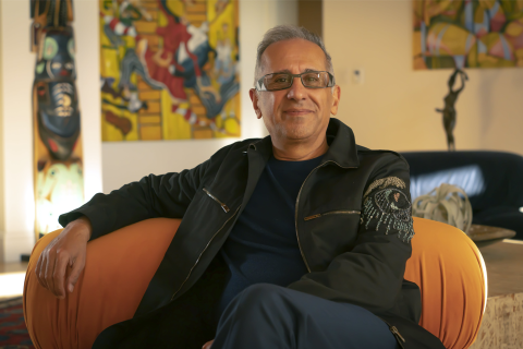 Siavash Alamouti smiles for the camera while seated in a room filled with vibrant artwork