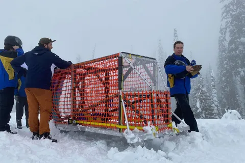 Four individuals in the snow with their concrete toboggan with trees in the background.