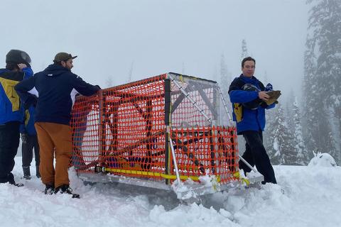 Four individuals in the snow with their concrete toboggan with trees in the background. 