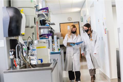 Two women in lab coats walking together in lab environment