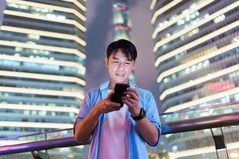 Man looking at his cell phone screen, standing in front of three tall buildings with bright lights