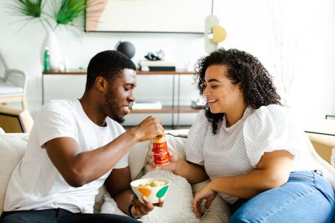 Black man and woman (romantic partners) sitting on a couch and sharing food