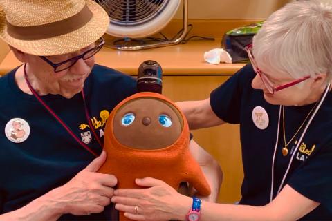 Mango, a social robot, looks sleepy while cradled in the arms of a senior man.