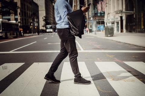 A man crosses a street while looking at his phone.