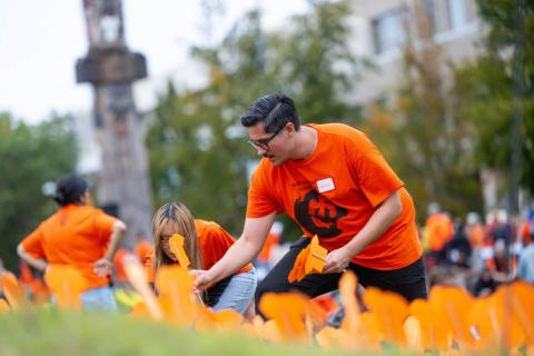 A man places a cutout of an orange shirt into the ground on Orange Shirt Day.