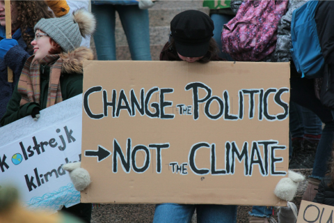 A protester holds a cardboard sign reading 'Change the Politics, Not the Climate' at a climate demonstration.