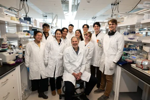 Dr. Peter Zandstra seated in a lab, surrounded by trainings, all wearing white lab coats.