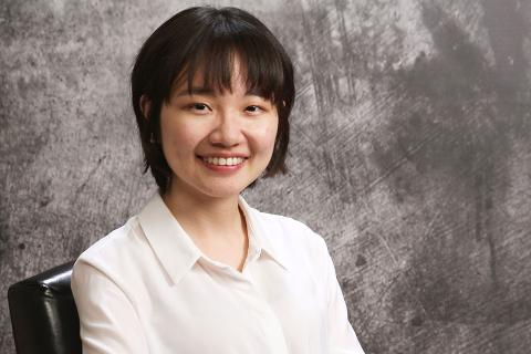 UBC MHLP Graduate Margaret Lin smiles for the camera while seated in front of a grey backdrop