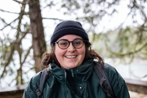 Image of Robyn Adams outdoors with trees in the background, wearing a black beanie and glasses