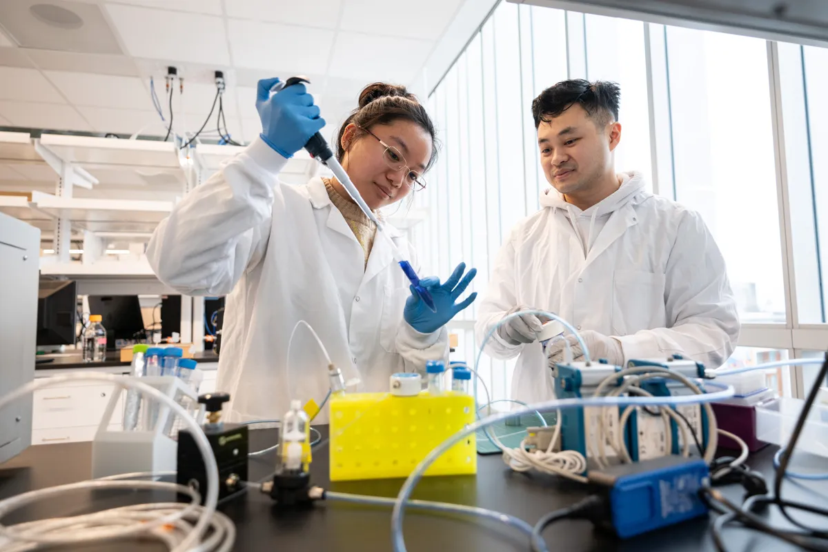 Two students wearing white coats in a lab