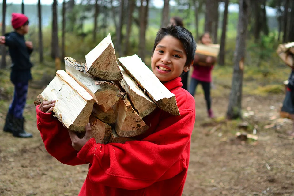 Geering Up student carrying a stack of wood in a forest