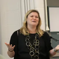 Woman in large ornate necklace speaking at lectern